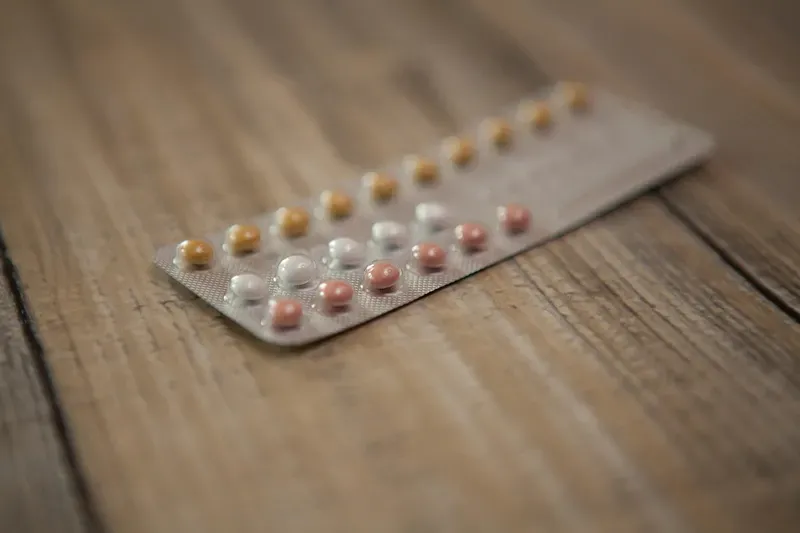 A blister pack of contraceptive pills on a wooden table, showing the daily pill format that emergency contraception pills differ from.